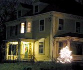 Old yellow house at night with lit tree and wreath on door