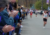 Street lined with people clapping as runners come towards us up hill