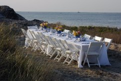 Table set with white tablecloth, silverware, etc., on the sand with sea in background