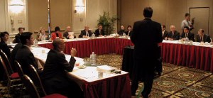 Many people around a U-shaped table listening to someone present