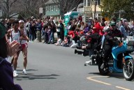 Crowd on both sides cheering two runners and motorcycle with a cropped closeup