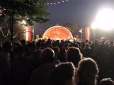 Back of people in a crowd facing orange semi-circle with TV lights facing us