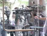 Row of 4 or 5 TV cameras on tripods seen through a glass door