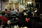 Dozens of people in chairs facing two people in a store