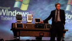 Jeff standing on stage next to table with about 10 Tablet PCs in front of Windows logo background