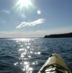 View from front seat of kayak of sparkling water with land jutting out in distance