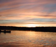 Colorful sunset above dark land with boat outline on water reflecting red/orange sky color