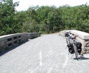 Gravel road going over bridge with bike and trees beyond