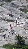Dozen or more people walking/climbing up huge flat rocks