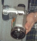Camera with long lens in hand, hanging around a neck next to part of flannel shirt