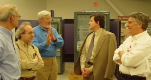 Five people standing talking in front of some very old computers in big racks