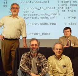 Four guys posing in front of projected listing