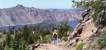 Mountain hiking trail with edge of lake in the crater in the background, Dan with hat and daypack seem from the rear