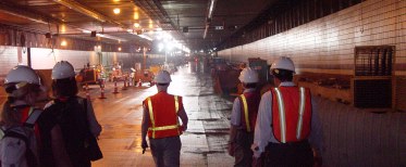 Looking into a tunnel lit with construction lights, lots of equipment, and people with hard hats and vests