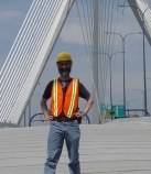 Dan with orange vest and hardhat with cables of the bridge visible