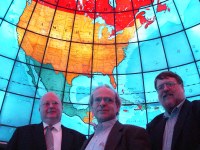 Three faces at the bottom in front of a bright, backlit, colorful image of North America