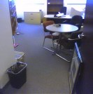 Looking in to an office with a round table, wastebasket, etc.