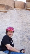John smiling with red helmet in front of steep smooth rock