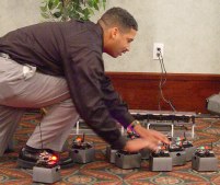 James leaning over with his hands on some of the 5x5x5 robots near something plugged into the wall