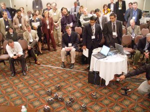 People standing a sitting watching robots together in a clump