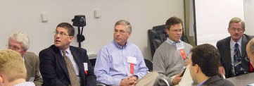 Left to right in order of speaking, sitting in chairs in front of the room