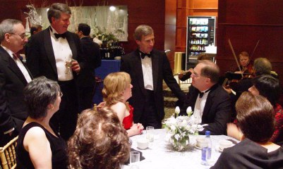 A small table with several people sitting around and a few standing looking at John