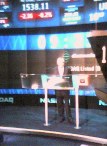 Mel alone at a plexiglass lectern