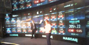 NASDAQ wall with lots of stocks showing and two people in front of it