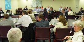 A few dozen people in chairs around tables in a medium sized conference room